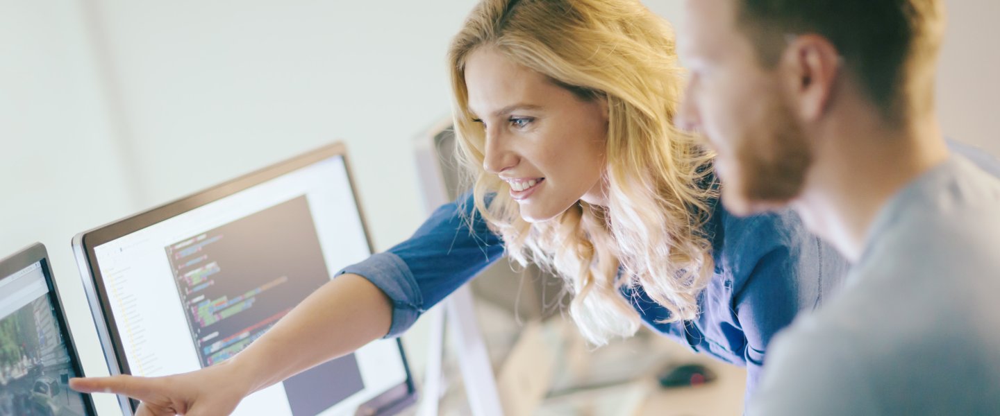Blonde Frau zeigt bei Gespräch am Arbeitsplatz auf Bildschirm